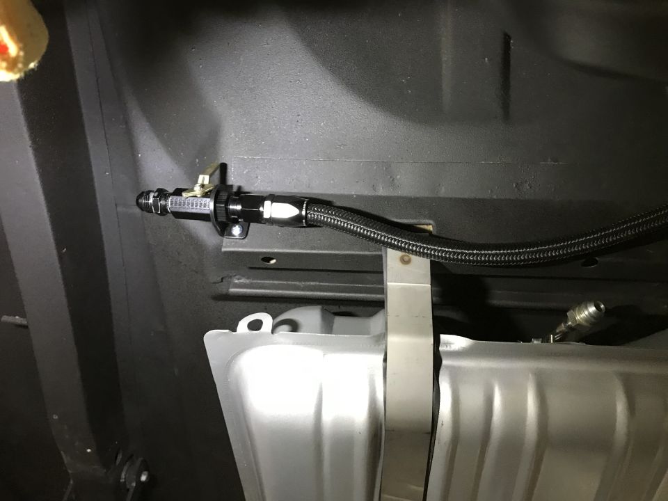 Close-up of a black braided fuel line with a shut-off valve mounted near a silver fuel tank.