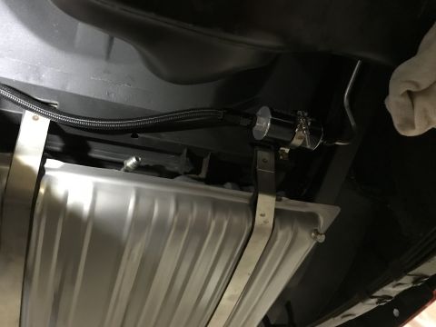 1964 Ford Fairlane - Underneath view of a fuel filter assembly attached to a metal fuel tank with straps. A braided fuel line runs from the left towards the fil…