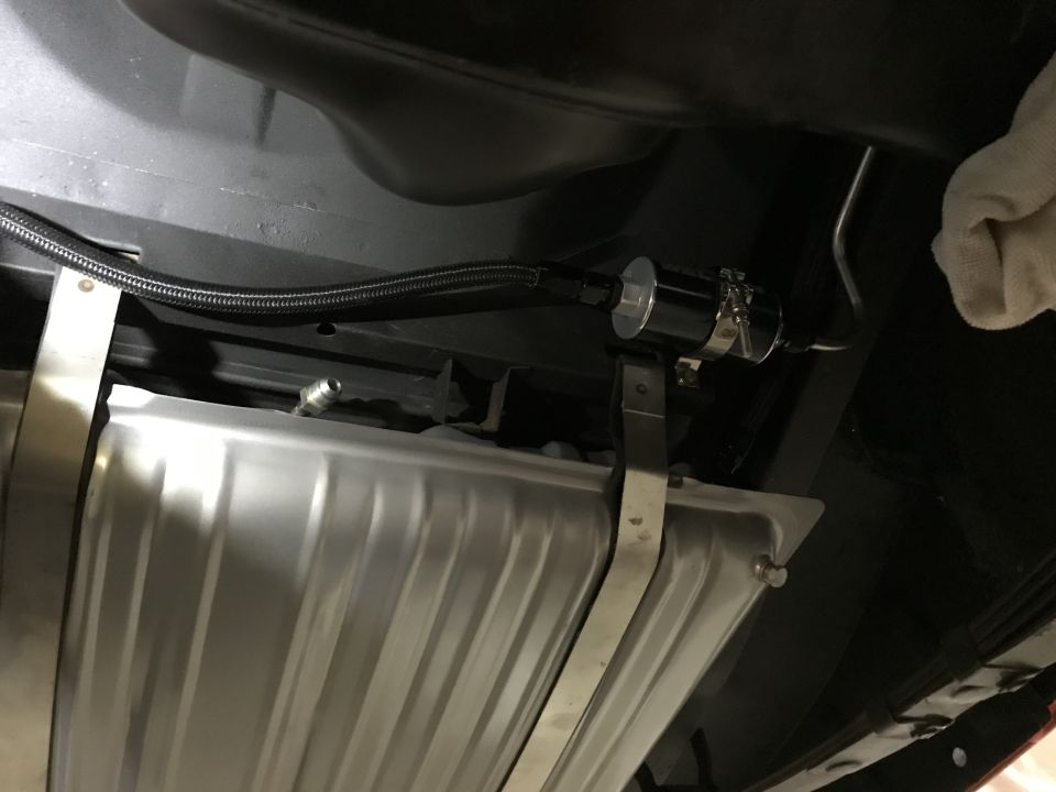 Underneath view of a fuel filter and braided fuel line attached to a metal fuel tank.