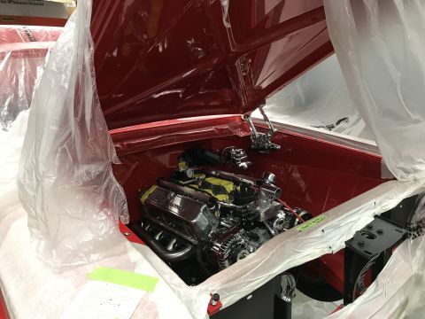 1964 Ford Fairlane - The engine bay of a red classic car, likely a 1964 Ford Fairlane, is covered with protective plastic sheeting. A chrome engine with yellow…