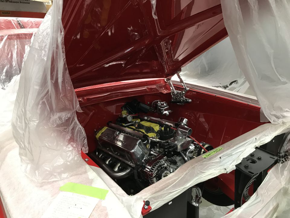Red classic car engine bay with chrome engine covered in plastic
