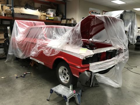 1964 Ford Fairlane - A red and white classic car, possibly a Ford Fairlane, is covered in protective plastic sheeting in a workshop. The hood is open, revealing…