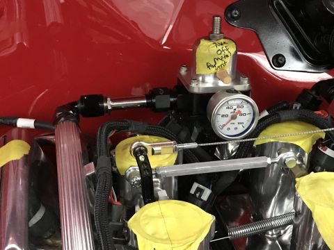 1964 Ford Fairlane - Close-up view of a fuel pressure regulator and gauge mounted on a red engine bay. A yellow sticky note with handwritten text is attached to…