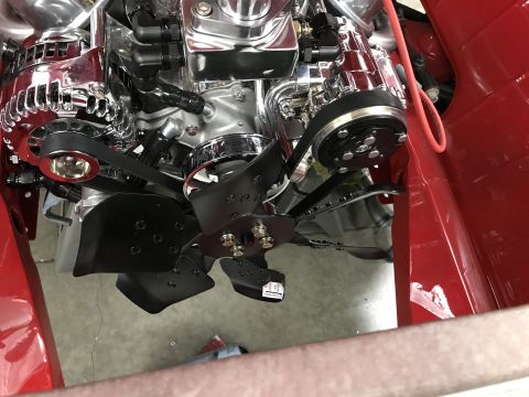 1964 Ford Fairlane - Close-up view of a polished chrome engine bay with a black fan and serpentine belt system. The engine is installed in a red vehicle.