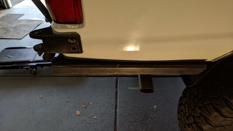 1995 Ford Bronco - A close-up view of the rear passenger side of a white vehicle, showing a custom metal step installed below the body and a portion of the ex…