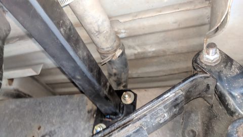 1995 Ford Bronco - The underside of a vehicle shows a black metal bracket bolted to the frame, with a hose clamp securing a rubber hose nearby. Another bracke…