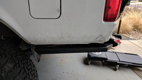 1995 Ford Bronco - The rear driver's side quarter panel and bumper of a white vehicle are shown. A black aftermarket bumper is installed, and there is visible…