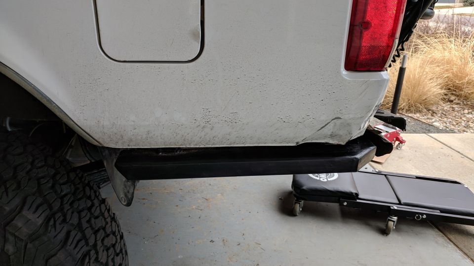 White vehicle's rear driver's side with black aftermarket bumper and body damage.