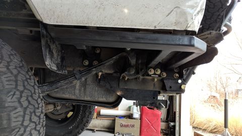1995 Ford Bronco - The underside of a white Ford Bronco shows a custom black metal rear bumper mount attached to the frame, with leaf springs and a fuel tank…