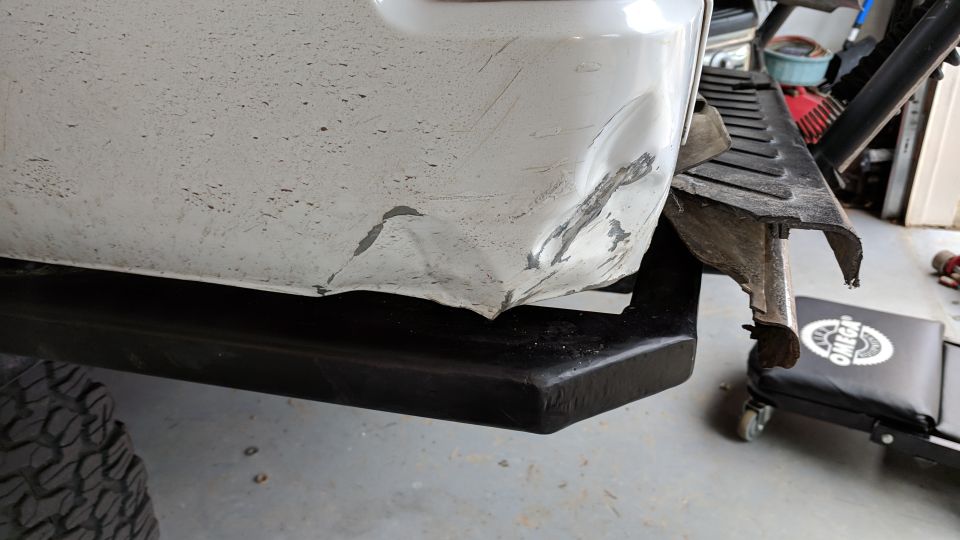 Damaged white rear bumper and fender on a vehicle with black step bar.