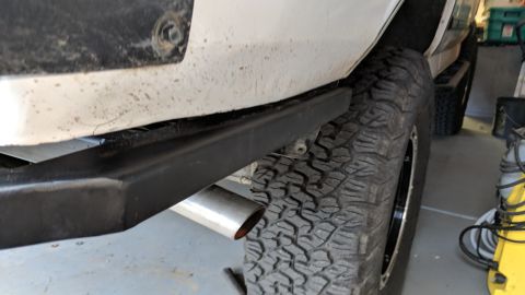 1995 Ford Bronco - Close-up view of the rear fender and tire of a white SUV, featuring a black rock slider and a chrome exhaust tip. The vehicle appears to be…