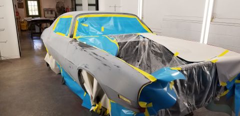 1970 Chevrolet Camaro - A classic car, likely a 1970s Chevrolet Camaro, is in a workshop being prepped for painting. The vehicle is heavily masked with blue plasti…