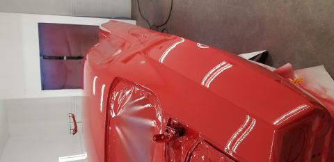 1970 Chevrolet Camaro - A bright red car, possibly a classic muscle car, is being worked on in a garage. Parts of the car are covered in protective plastic wrap, a…