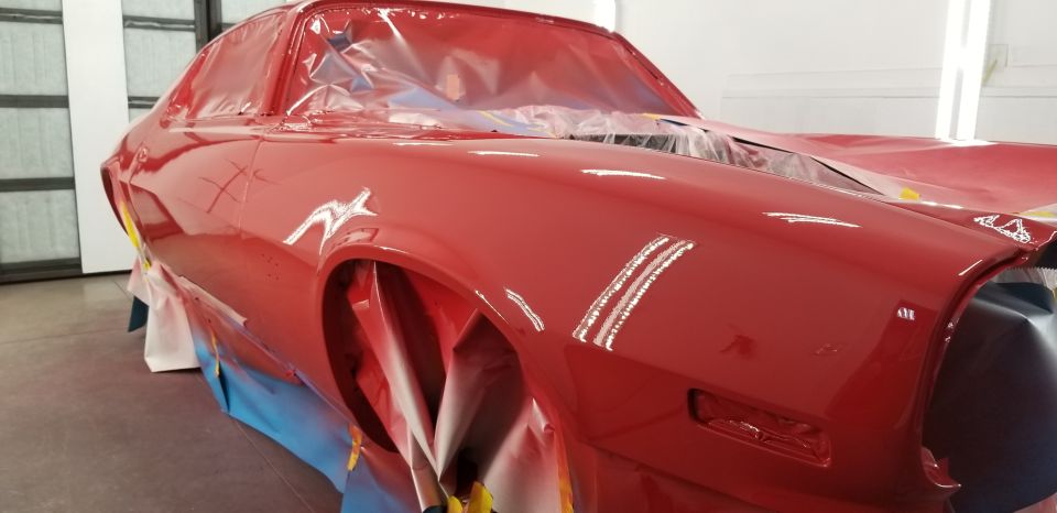 Close-up of a red classic coupe with protective plastic and masking.