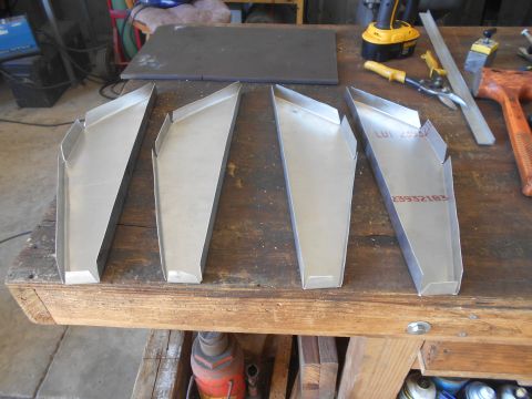 1992 Ford Bronco - Four custom-bent sheet metal parts are laid out on a wooden workbench. Two of the parts have red stamped text on them.