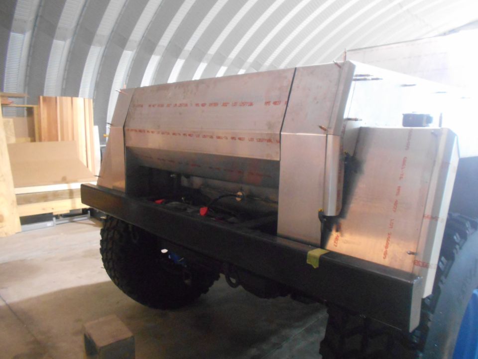 Custom aluminum truck bed with off-road tire, mounted on a black frame, indoors.