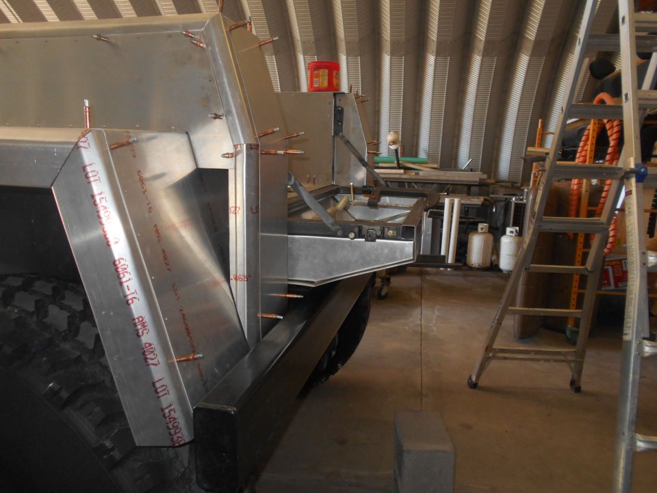 Custom aluminum body panels being riveted onto a vehicle in a workshop.