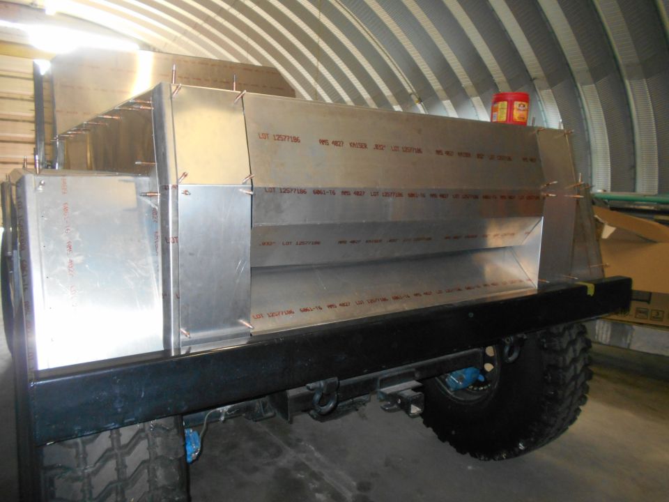 Aluminum body panels riveted together on a vehicle chassis, with large off-road tires visible