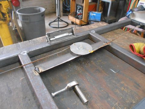 1992 Ford Bronco - A metal frame assembly with a ratchet and a circular metal component is shown on a workbench.
