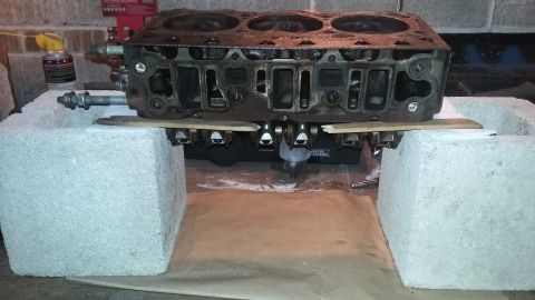Engine cylinder head resting on concrete blocks, with visible bolts and internal components