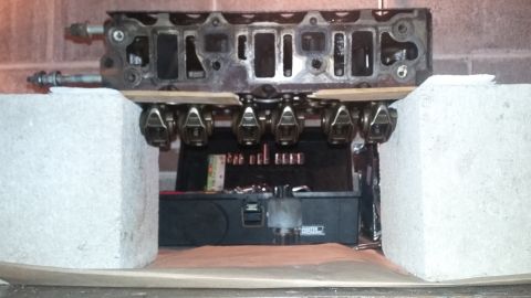 Engine cylinder head with visible valves and rockers, supported by concrete blocks