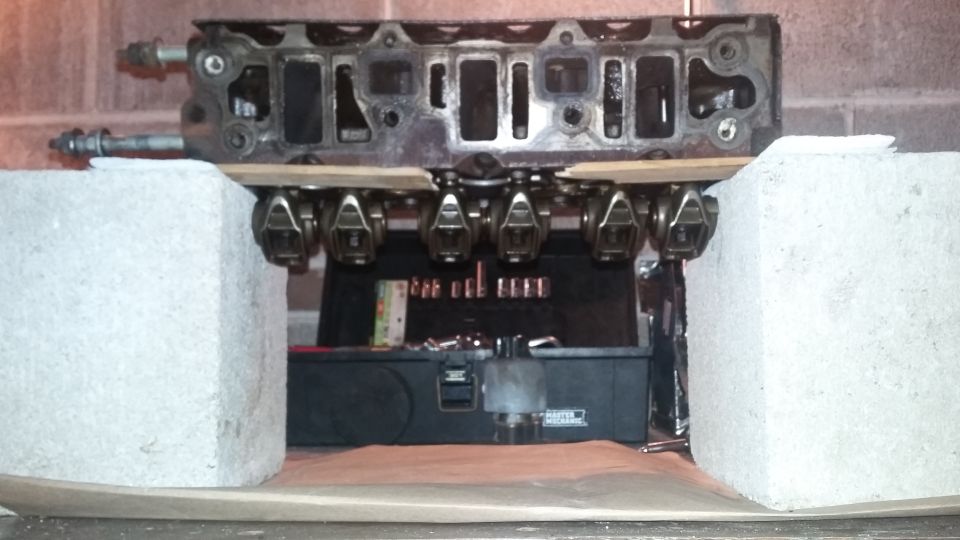 Engine cylinder head with visible valves and rockers, supported by concrete blocks