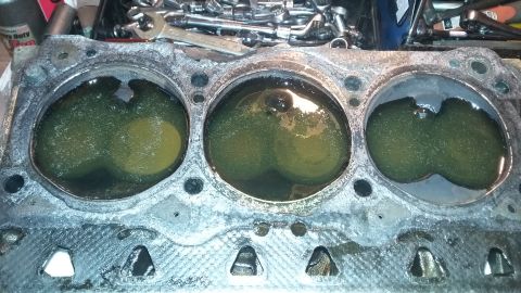Engine cylinder head with three cylinders filled with green liquid, tools in background