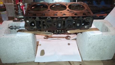 Engine cylinder head resting on concrete blocks with wrenches below