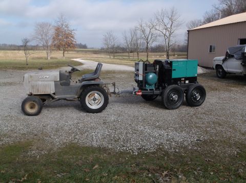 1984 Honda ATC 250 R - A White riding mower tows a generator unit on a gravel surface near a building and a pickup truck.