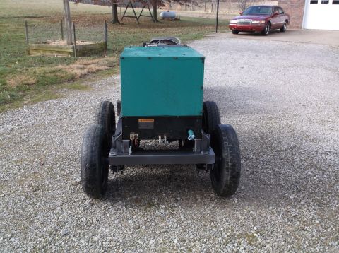 1984 Honda ATC 250 R - A generator unit with wheels is parked on a gravel driveway, with a red car in the background.