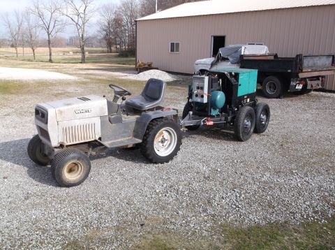 1984 Honda ATC 250 R - A White riding mower is hitched to a trailer carrying a generator, with a dump truck parked behind it.