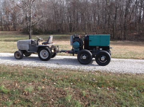 1984 Honda ATC 250 R - A tractor tows a large green generator unit on a gravel driveway in a rural setting.