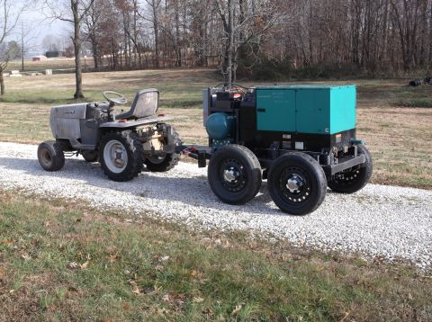 1984 Honda ATC 250 R - A tractor tows a generator unit across a gravel driveway in a rural setting.