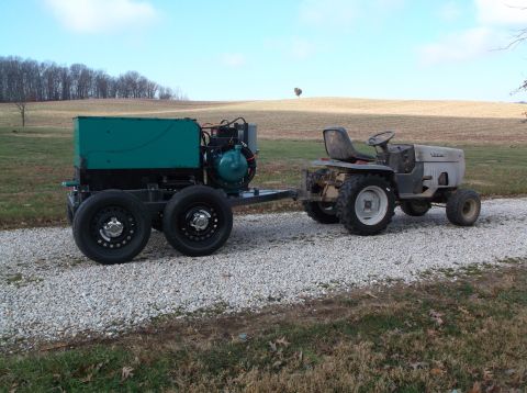 1984 Honda ATC 250 R - A portable generator is towed by a garden tractor on a gravel road with a field in the background.