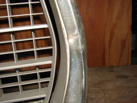 1973 Ford Ranchero - Close-up of a dented chrome bumper section next to a white plastic grille.