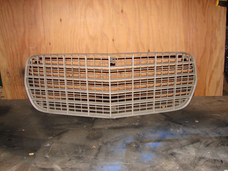 Gray car grille with horizontal bars and a V-shaped center, mounted on a wooden background