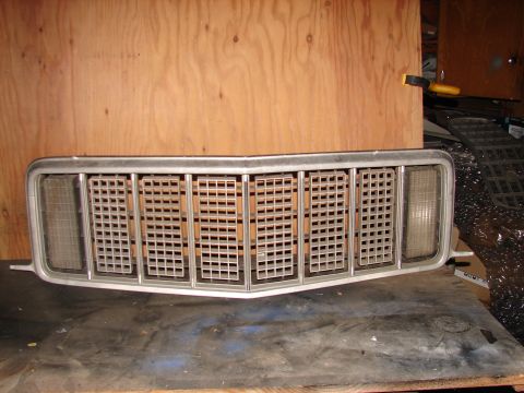 1973 Ford Ranchero - A vehicle grille is shown resting on a wooden surface against a plywood background.