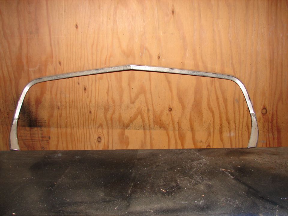 Chrome trim piece with a V-shaped bend in the center, against a wood-paneled background