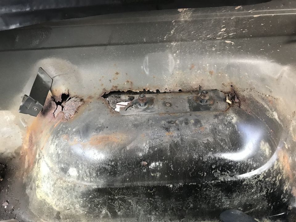 Rusted vehicle floor pan with a metal bracket and holes from corrosion