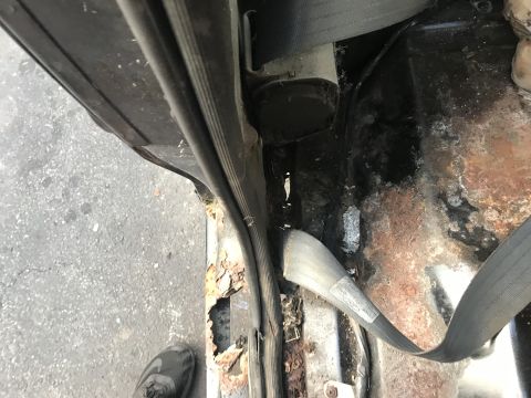 1992 Ford Bronco - Detail of a rusted floor pan and door frame, with a seatbelt visible.