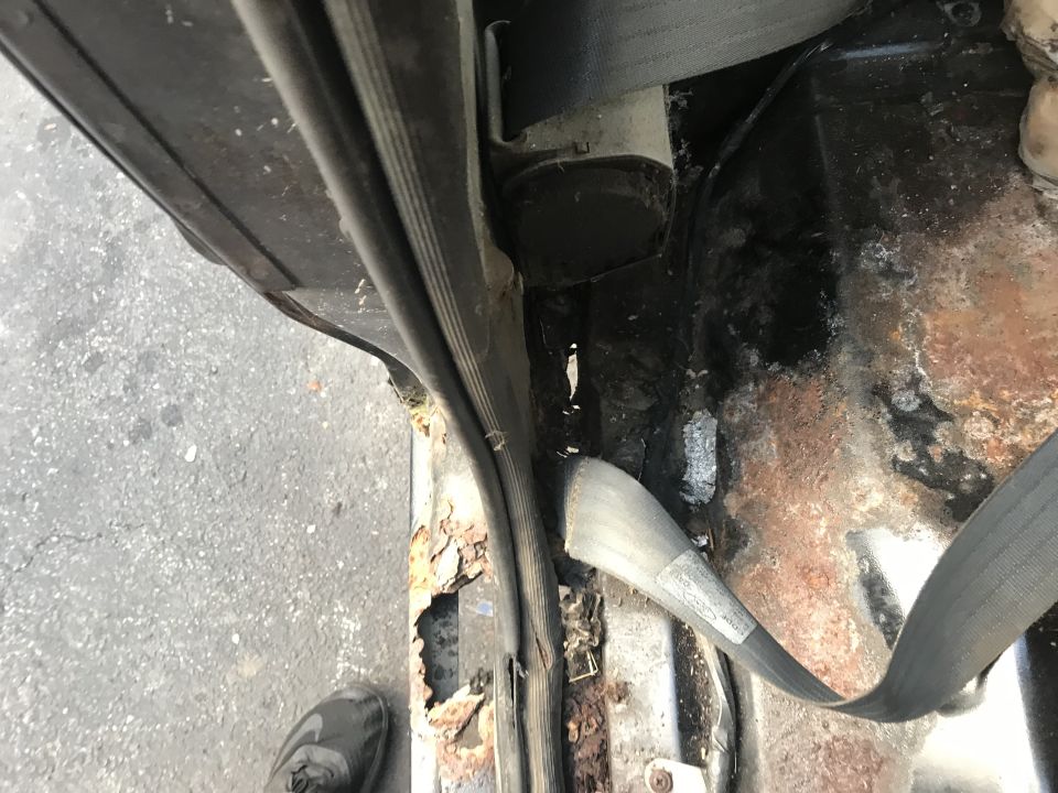 Interior door frame and rusted floor pan with seatbelt