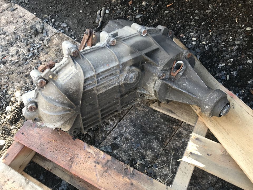 Gray metal transfer case with bolts and flanges, resting on wooden pallets