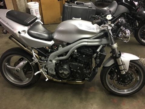 2000 Ford E350 - Silver Triumph Speed Triple motorcycle parked indoors next to another motorcycle.