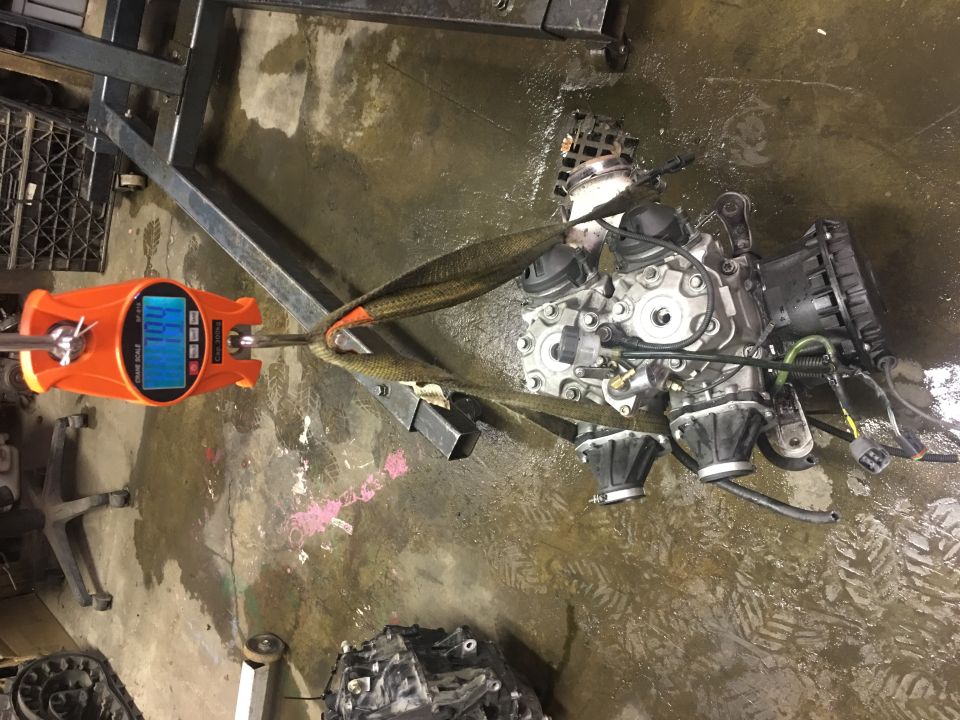Orange digital scale weighing an engine assembly with straps, showing 109 lbs