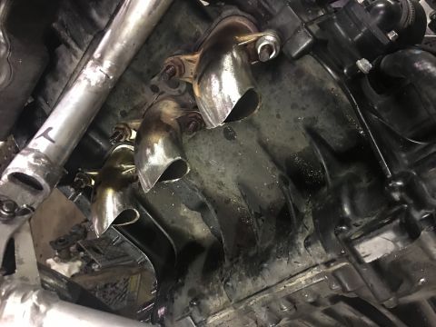 2000 Ford E350 - Close-up view of exhaust manifold pipes connected to a black engine block, with some visible text on a metal pipe.