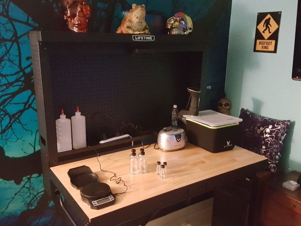 Workbench setup with scales, bottles, a small appliance, and decorative skulls. Bigfoot crossing sign on wall