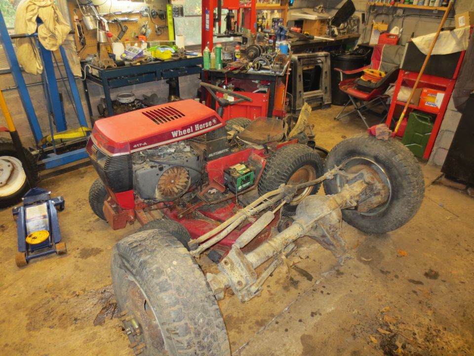 Red Wheel Horse riding mower with engine exposed and rear axle removed, in a cluttered garage