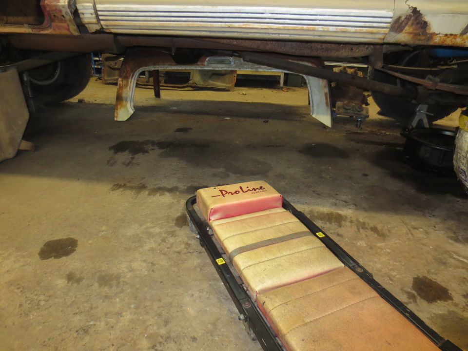 Underbody of a vehicle, showing frame and suspension components, with a red and tan creeper in the foreground