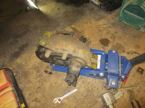 1967 Ford F-250 - A removed transfer case rests on a jack, surrounded by tools in a garage setting.