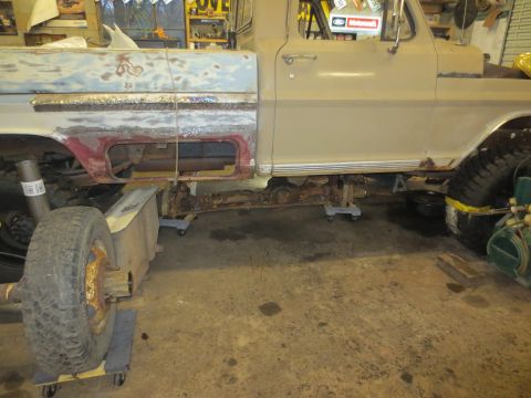 1967 Ford F-250 - The side of a 1967 Ford F-250 pickup truck is shown with its frame and drivetrain exposed for repair work.